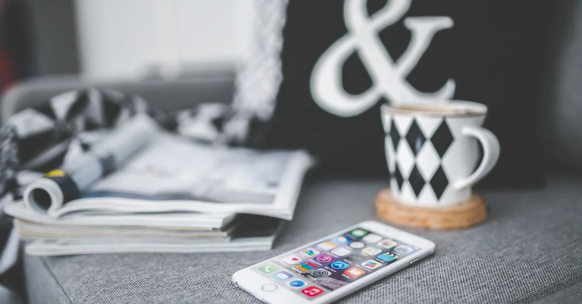 Un smartphone à côté d'une tasse de café élégante et de magazines dans un cadre de canapé confortable.