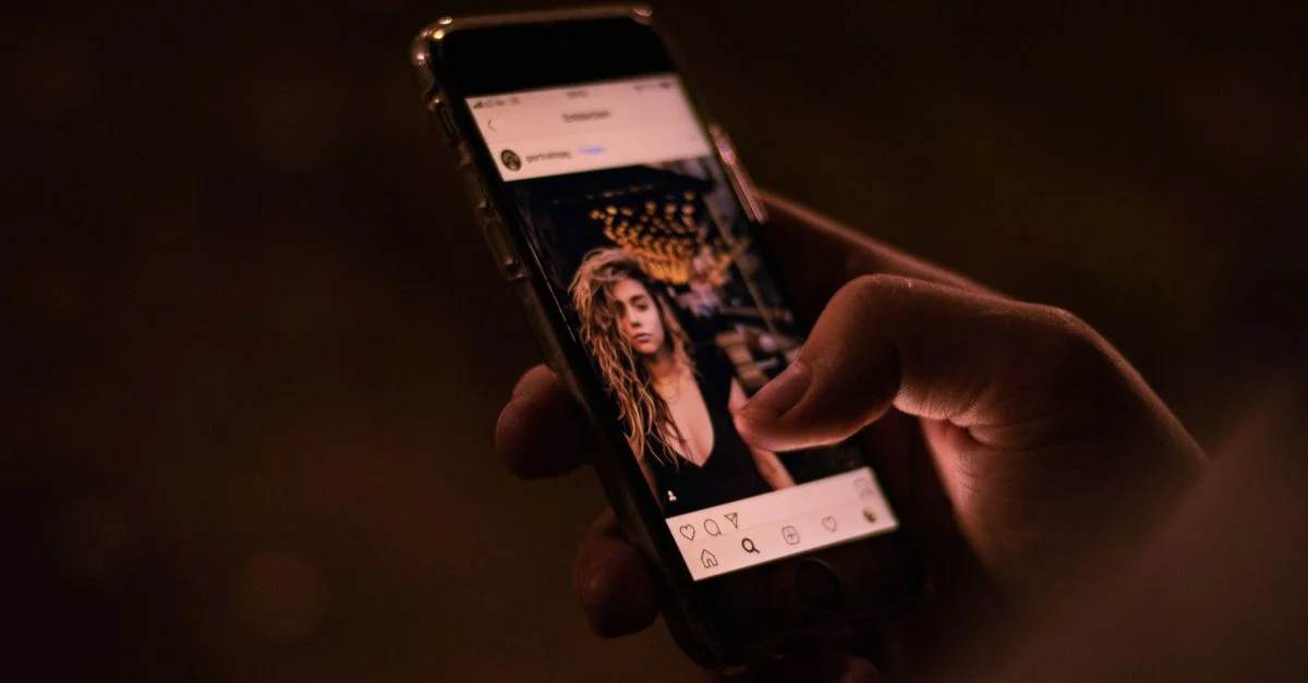 Gros plan d'une main interagissant avec un smartphone, naviguant sur les réseaux sociaux la nuit.