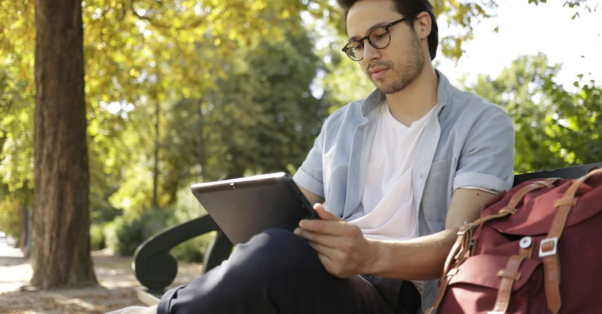 Jeune homme détendu lisant une tablette en plein air dans un parc ensoleillé.