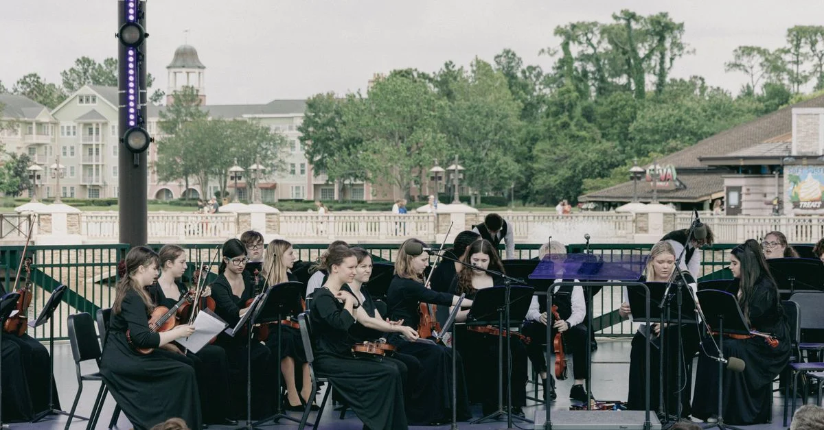 Concert en plein air d'orchestre avec des musiciens et des instruments à cordes dans un cadre de scène.