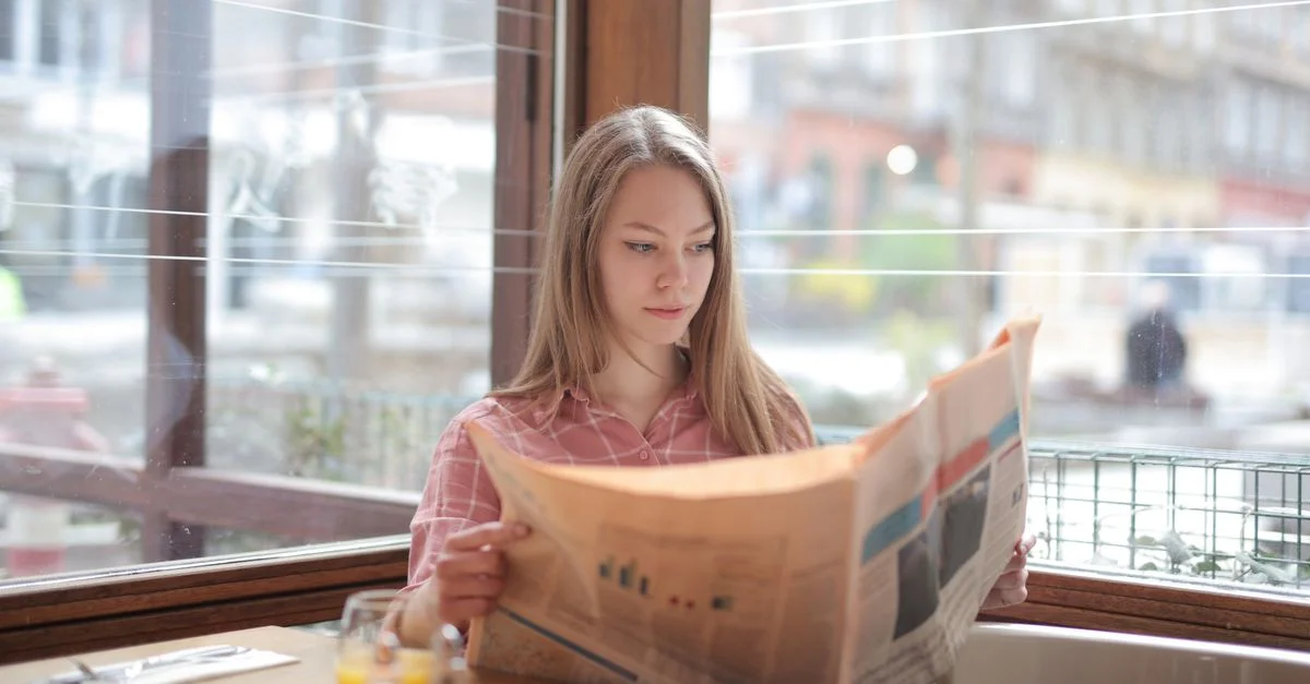 Une jeune femme profitant d'un journal à une table de café, plongée dans sa lecture.