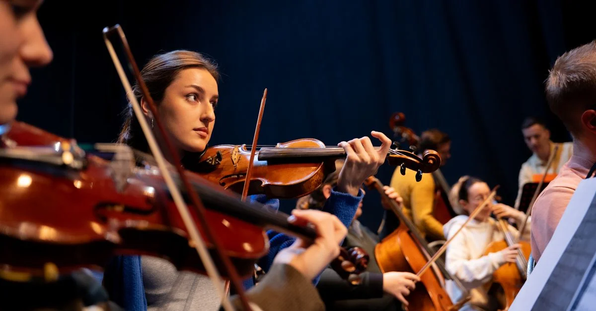 Un groupe de musiciens se produit dans un orchestre, mettant en avant un violoniste.