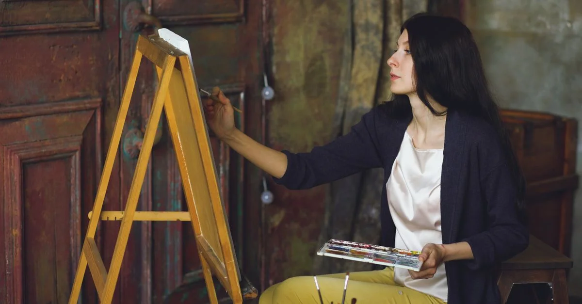 Artiste féminine concentrée sur la peinture d'une toile à l'intérieur, mettant en valeur sa créativité.
