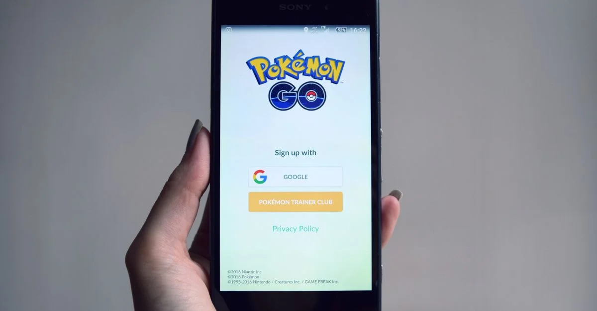 Smartphone affichant l'écran de connexion de l'application Pokémon Go, tenu en main.