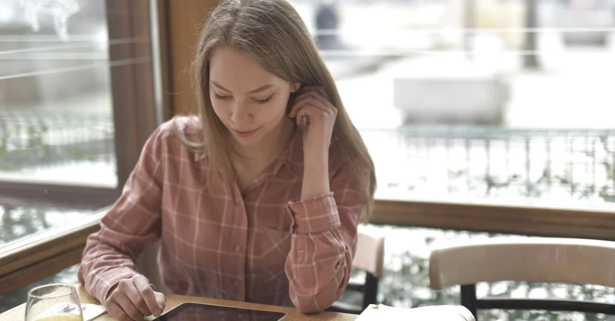 Une jeune femme se détend avec une tablette et un jus d'orange dans un café chaleureux.